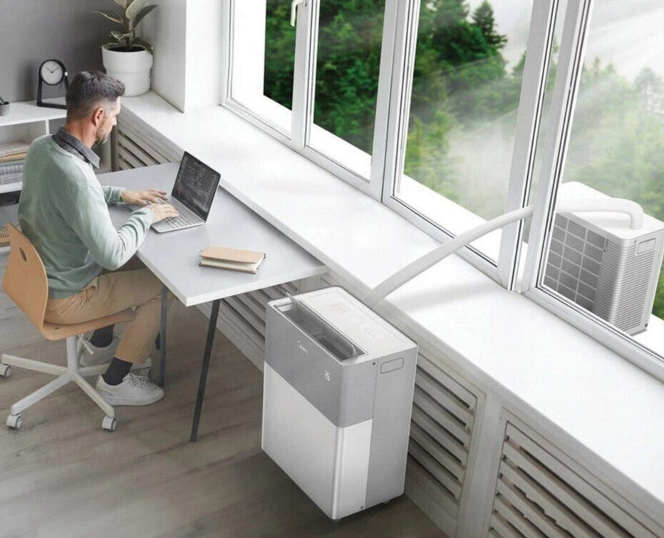 Person working at a desk with a laptop, air purifier on the floor, and air conditioning unit in the background.